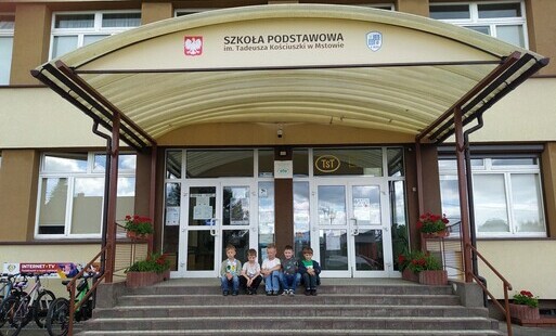 Chłopcy siedzący na schodach przed budynkiem szkoły